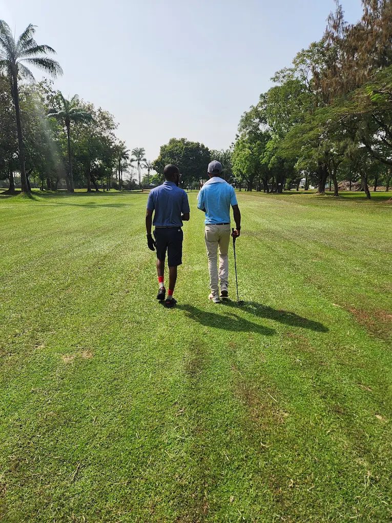 Two golfers walking down a tree-lined fairway at Ikeja